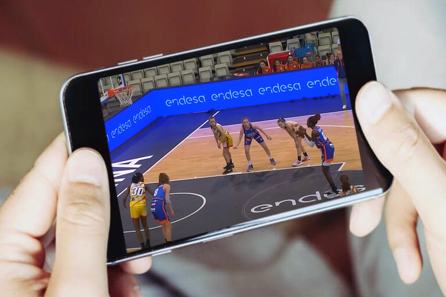 Manos sosteniendo un teléfono de retransmisión en directo de partido de básquet femenino