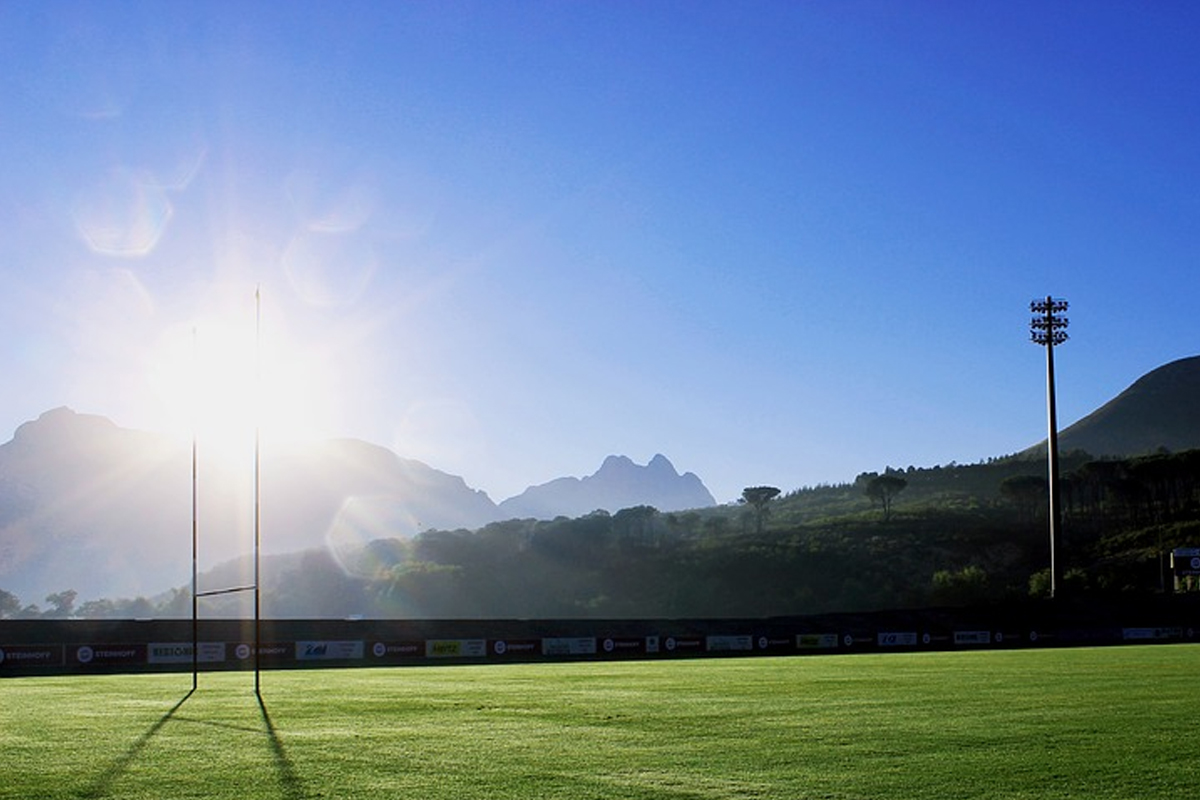 Plano general de un campo de rugby con montañas de fondo y cielo azul