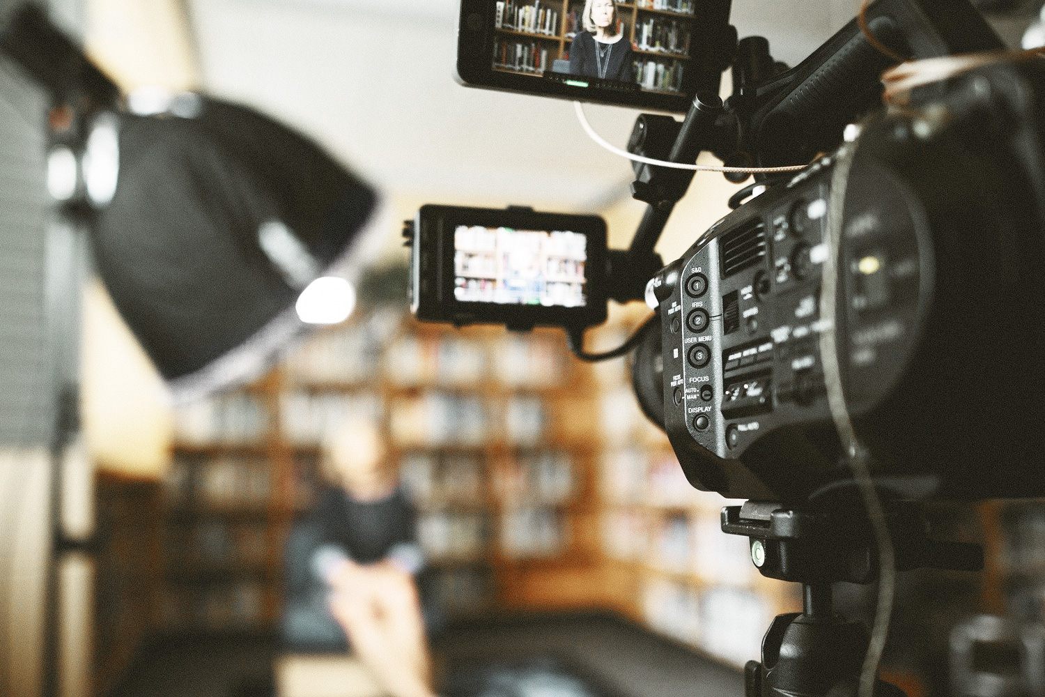 Plano detalle de cámara profesional grabando streaming en directo de mujer con estanterías de fondo